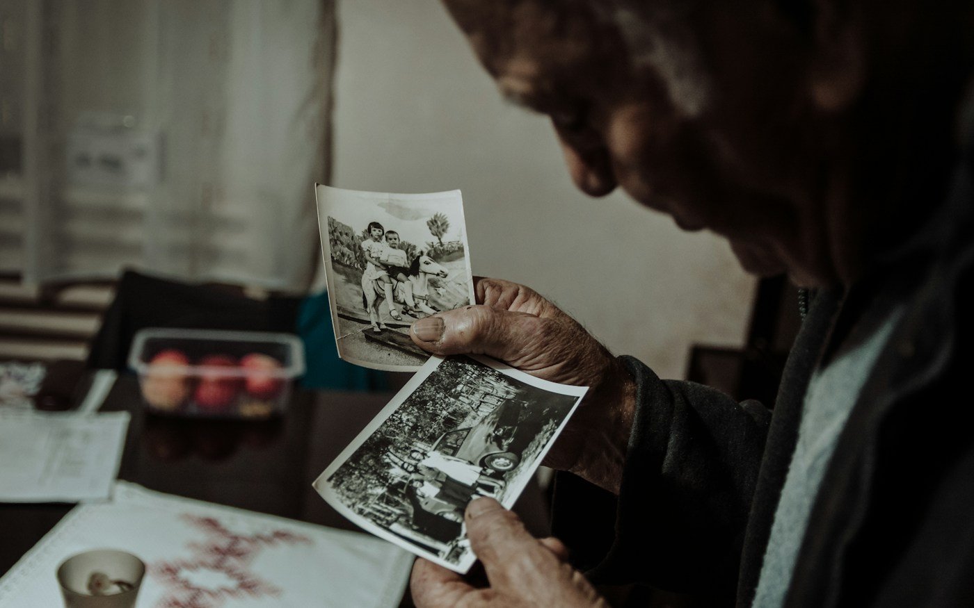 Stariji muškarac drži i promatra stare obiteljske fotografije.
